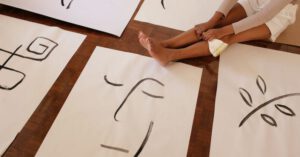 Hobby Family - From above of faceless barefoot casually dressed woman with brush sitting on floor while placed artworks in abstract style
