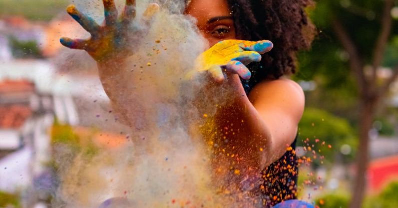Creative Play - Anonymous African American female squatting on tile pavement with hands apart while playing with multicolored dry paints during Hindu Festival of Colors under cloudy sky