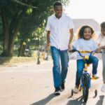 Happy Family - Man Standing Beside His Wife Teaching Their Child How to Ride Bicycle