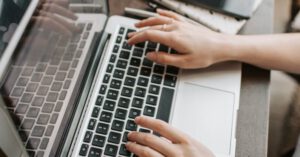 Independent Creativity - From above of unrecognizable woman sitting at table and typing on keyboard of computer during remote work in modern workspace