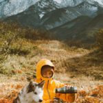 Pets Weather - Full body frozen traveler resting on grassy highland with adorable Husky dog and pouring hot drink from thermos bottle against majestic snowy mountain range on cold day