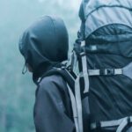 Travel Safety - Man Wearing Black Hoodie Carries Black and Gray Backpacker Near Trees during Foggy Weather