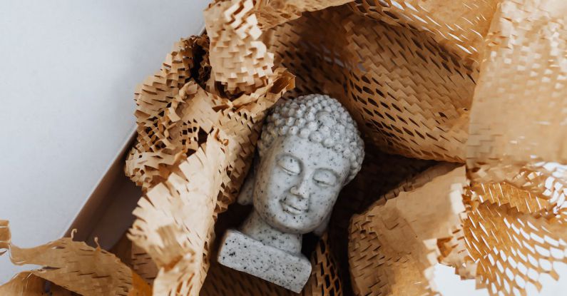 Online Safety - Top view of gray stone bust of Buddha placed on white marble table in cardboard box with craft perforated paper after receiving postal delivery