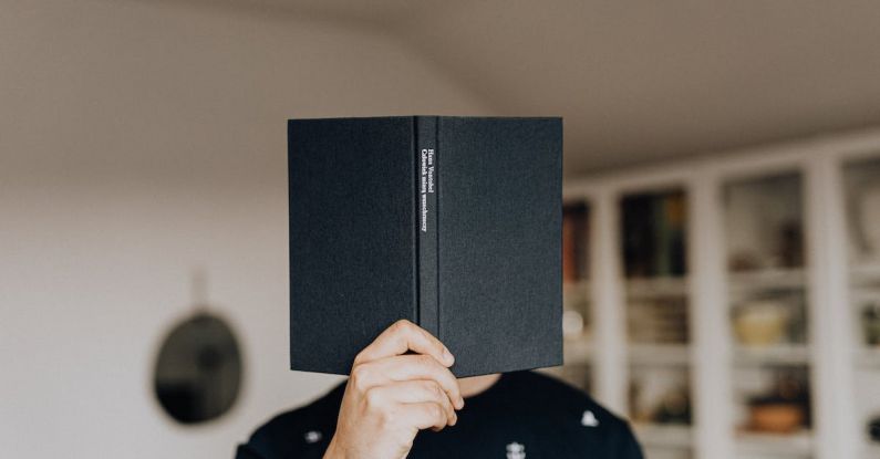 Science Home - Faceless male holding opened black book in hand covering face while standing in middle of light room