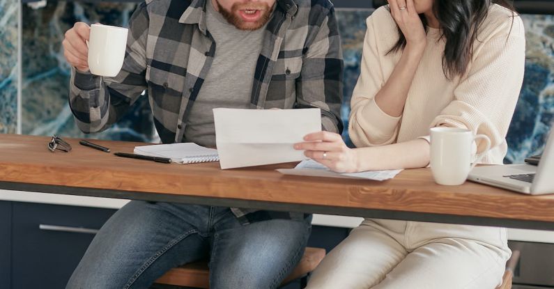 Couples Finance - A Couple Sitting Near the Wooden Table while Looking at the Document in Shocked Emotion