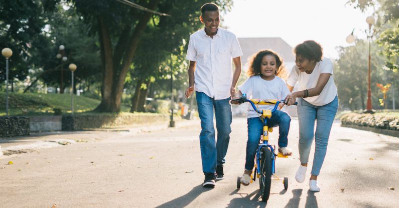 Happy Family - Man Standing Beside His Wife Teaching Their Child How to Ride Bicycle