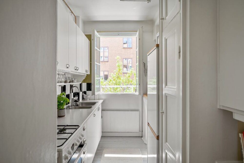 A bright and contemporary small kitchen with white cabinets and open window.
