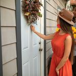 A man and a woman knocking on a door decorated with a wreath, holding flowers.